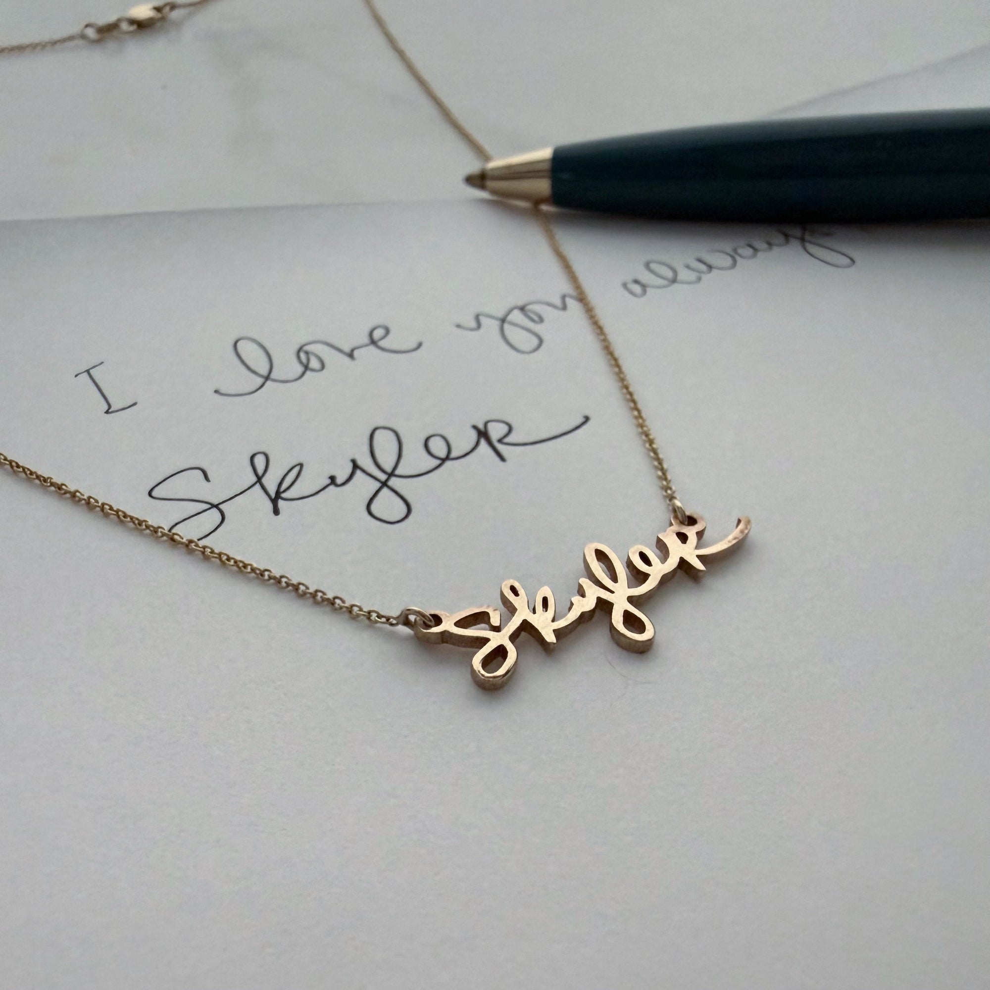 A handwritten note paired with a gold necklace shaped from the same script, showing the transformation of handwriting into fine jewelry.