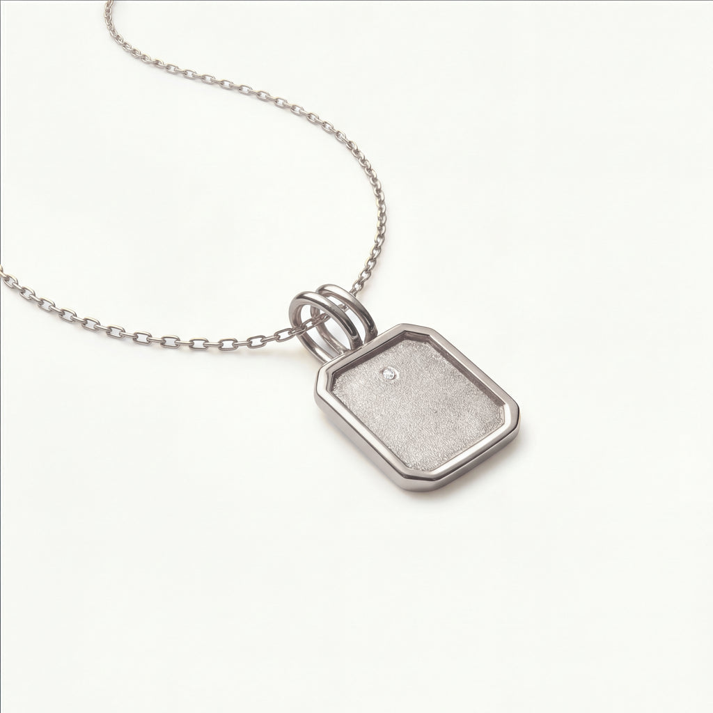 Macro view of the Bria pendant in 14k white gold, showcasing the signature sandblast finish and a bezel-set diamond on a streamlined, fine-link chain.