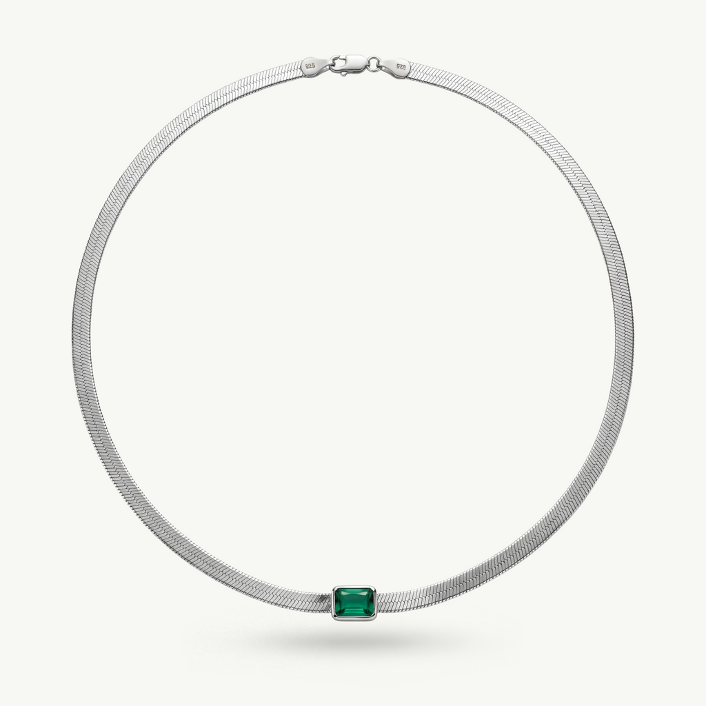 A sterling silver herringbone chain necklace featuring a bezel-set emerald green gemstone, designed with a minimal and architectural aesthetic.